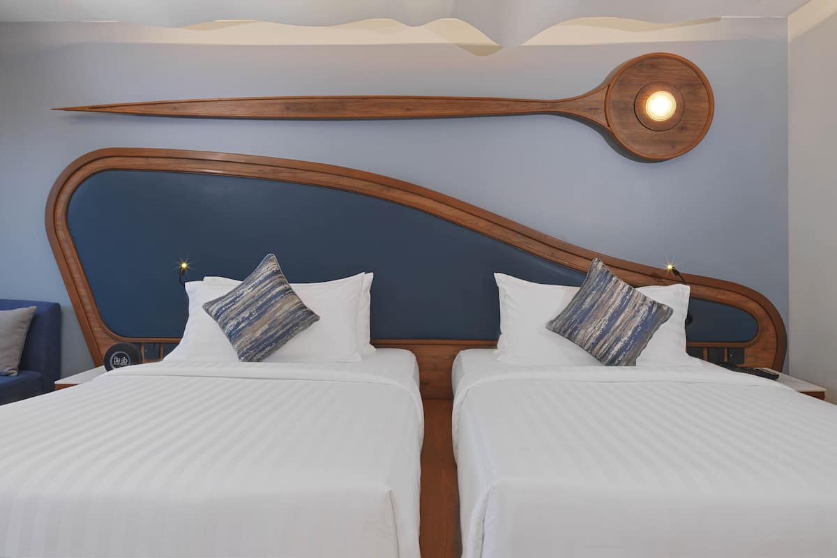 A hotel room with two beds, a wooden headboard, and a unique wall-mounted light fixture.