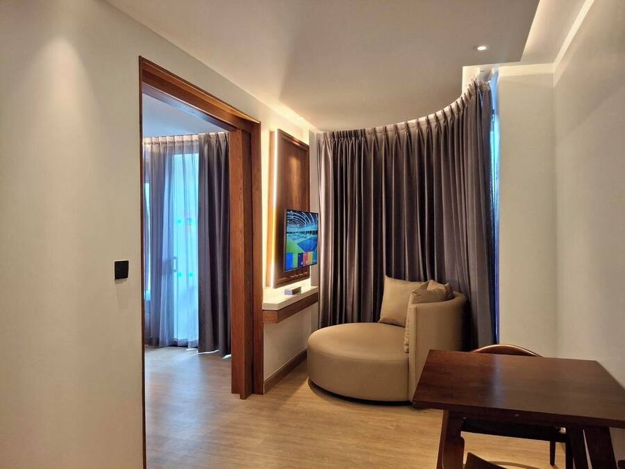 Una moderna camera d'albergo con un divano curvo, un tavolo in legno e un televisore a schermo piatto fissato al muro.