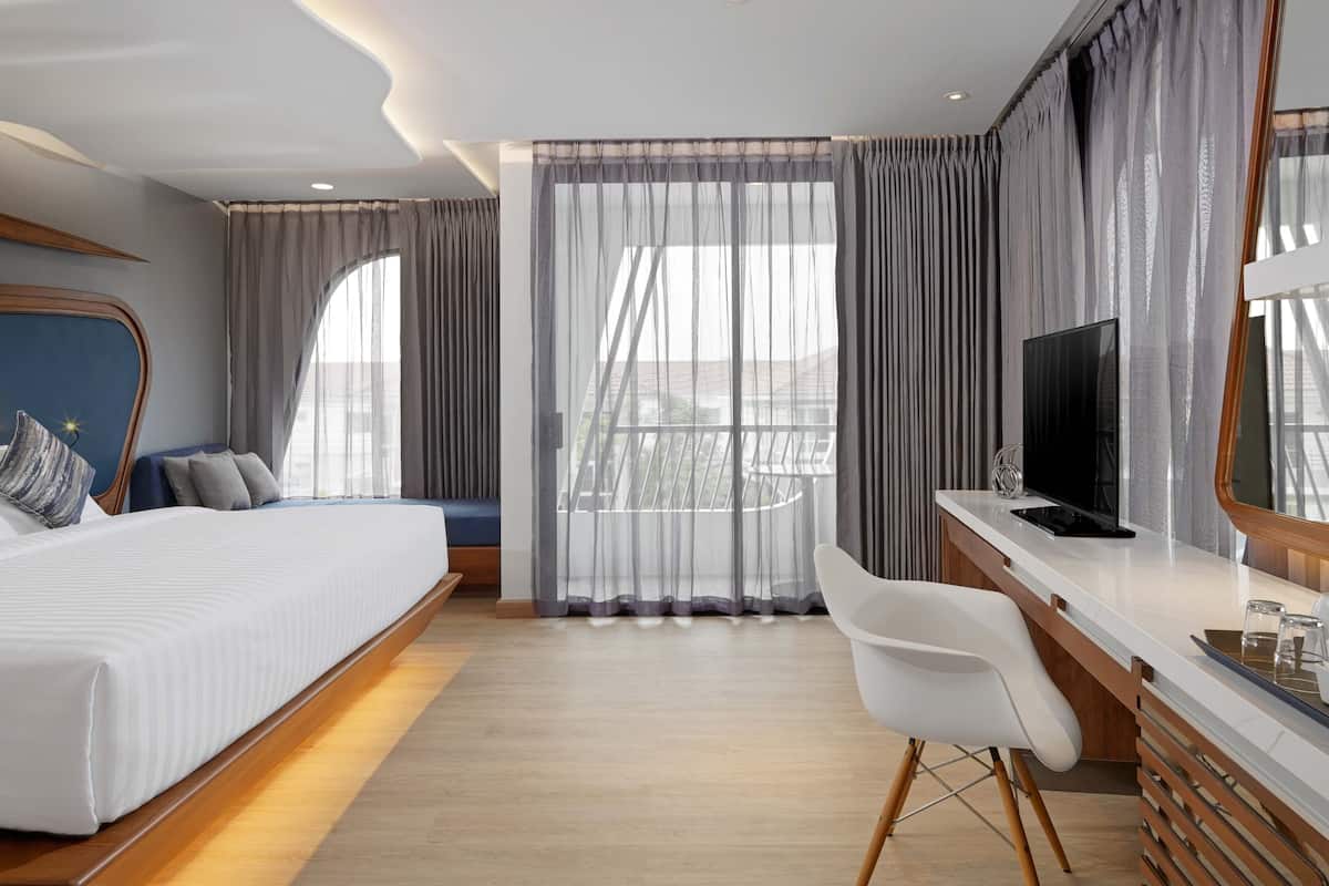A modern hotel room with a large bed, a desk with a TV, and a balcony view.