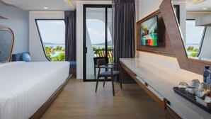 Quarto de hotel moderno com cama, escrivaninha, cadeira, televisão e varanda vista para o mar.