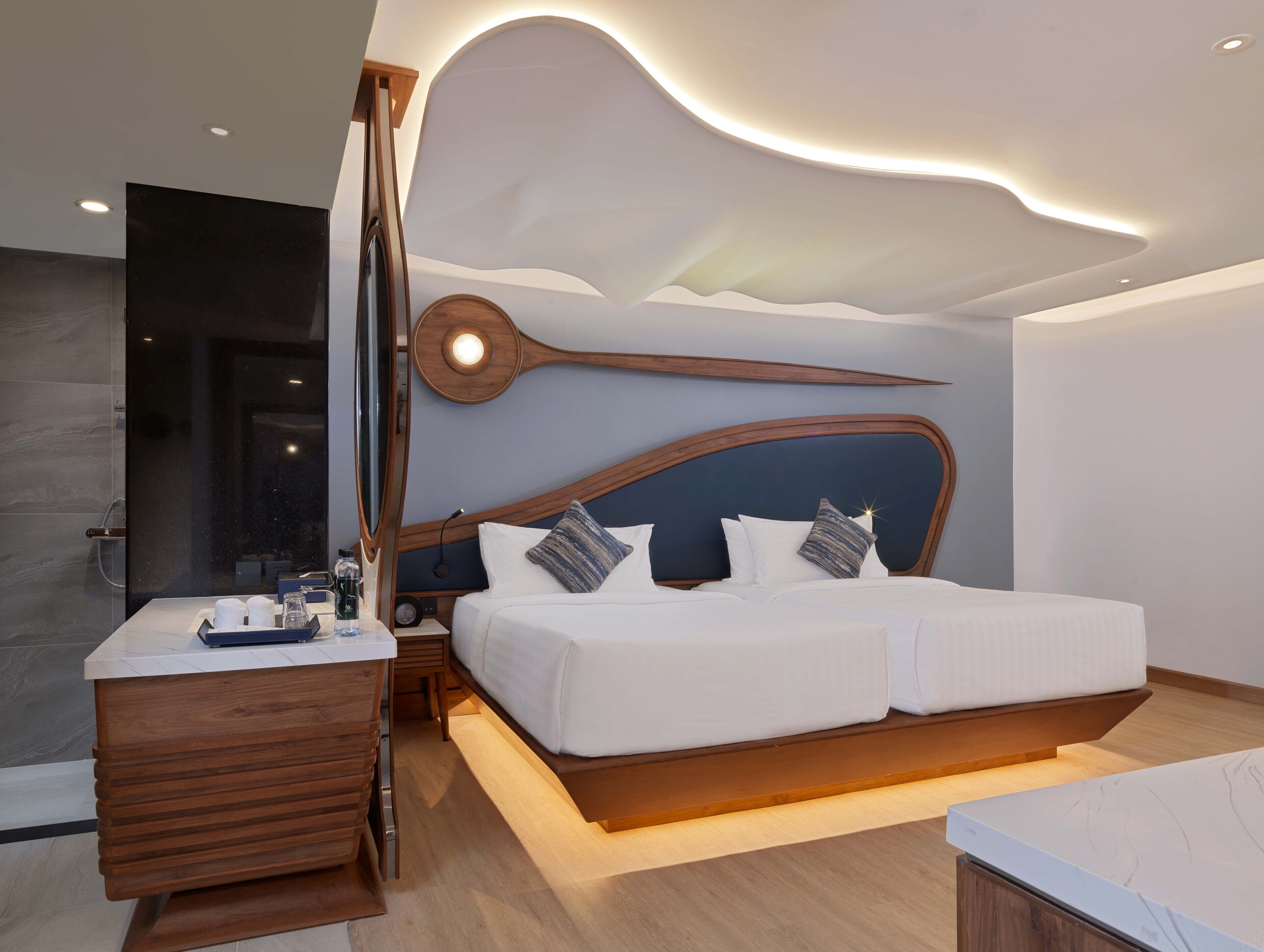A modern bedroom with a large bed, wooden headboard, bedside tables, and a built-in desk with a mirror.