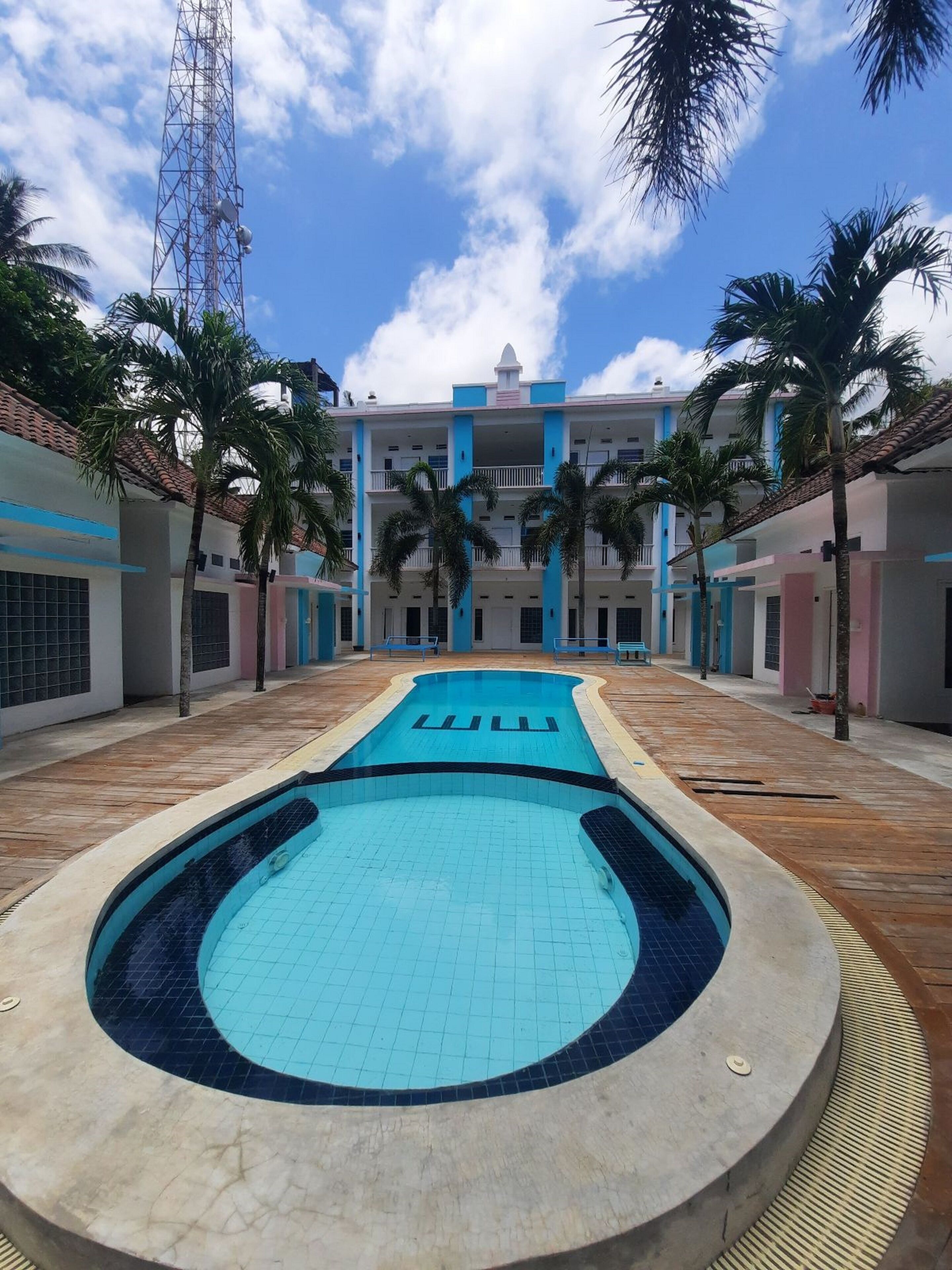 Ein Pool mit gefliestem Deck, umgeben von Palmen und Gebäuden mit blau-weißen Fassaden.
