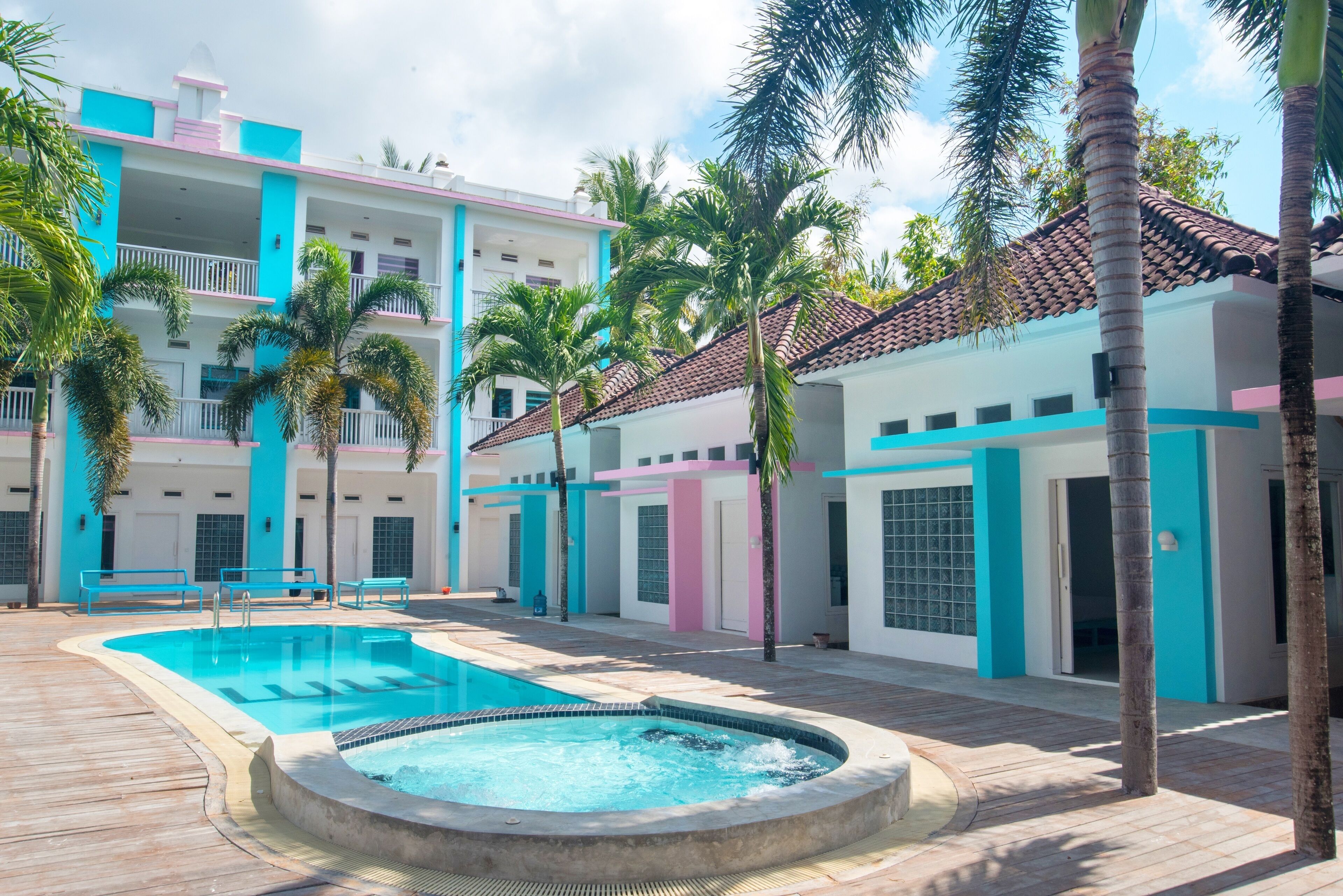A pool area with a hot tub, palm trees, and a building with balconies and a tiled roof.