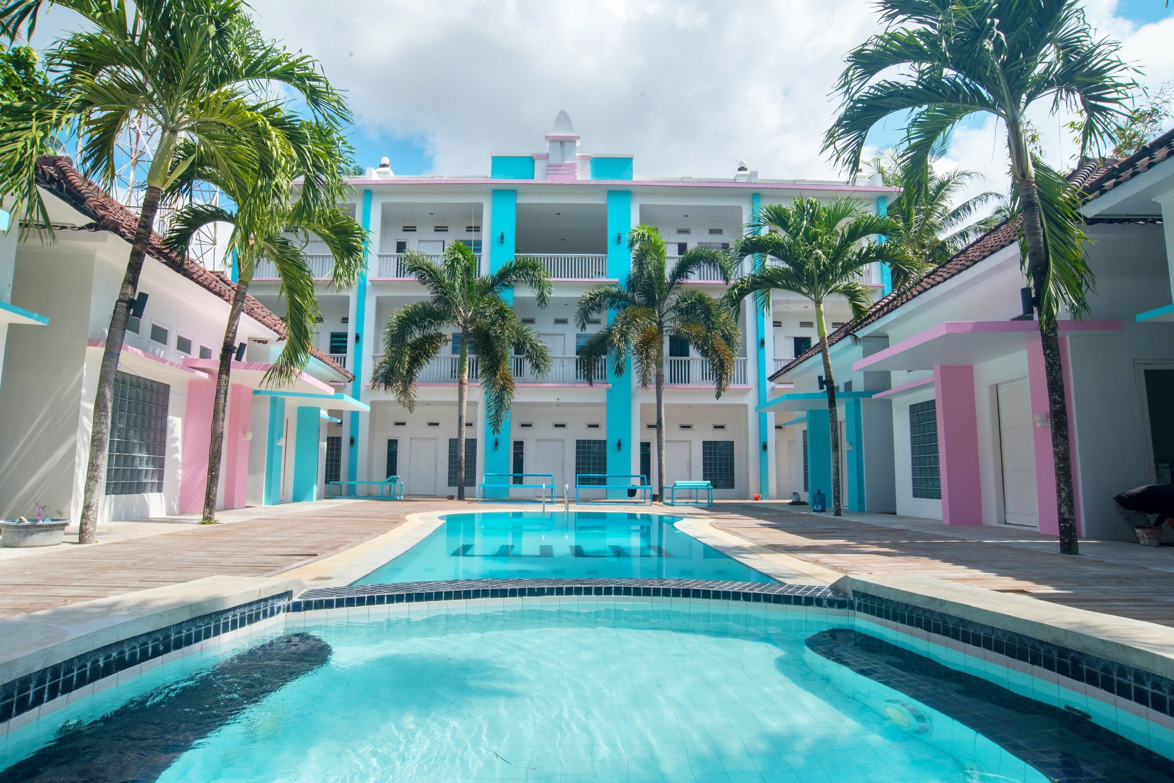 A swimming pool surrounded by palm trees and a multi-story building with balconies.