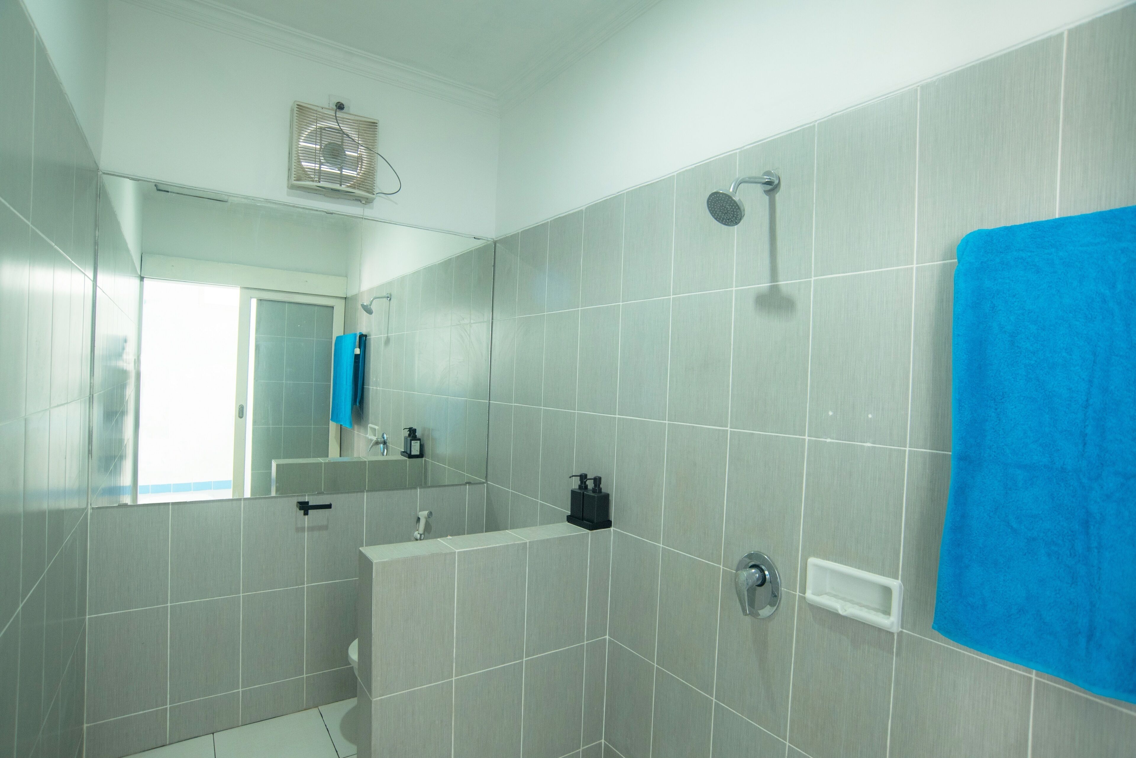 A modern bathroom with grey tiles, a blue towel, a mirror, and a shower.