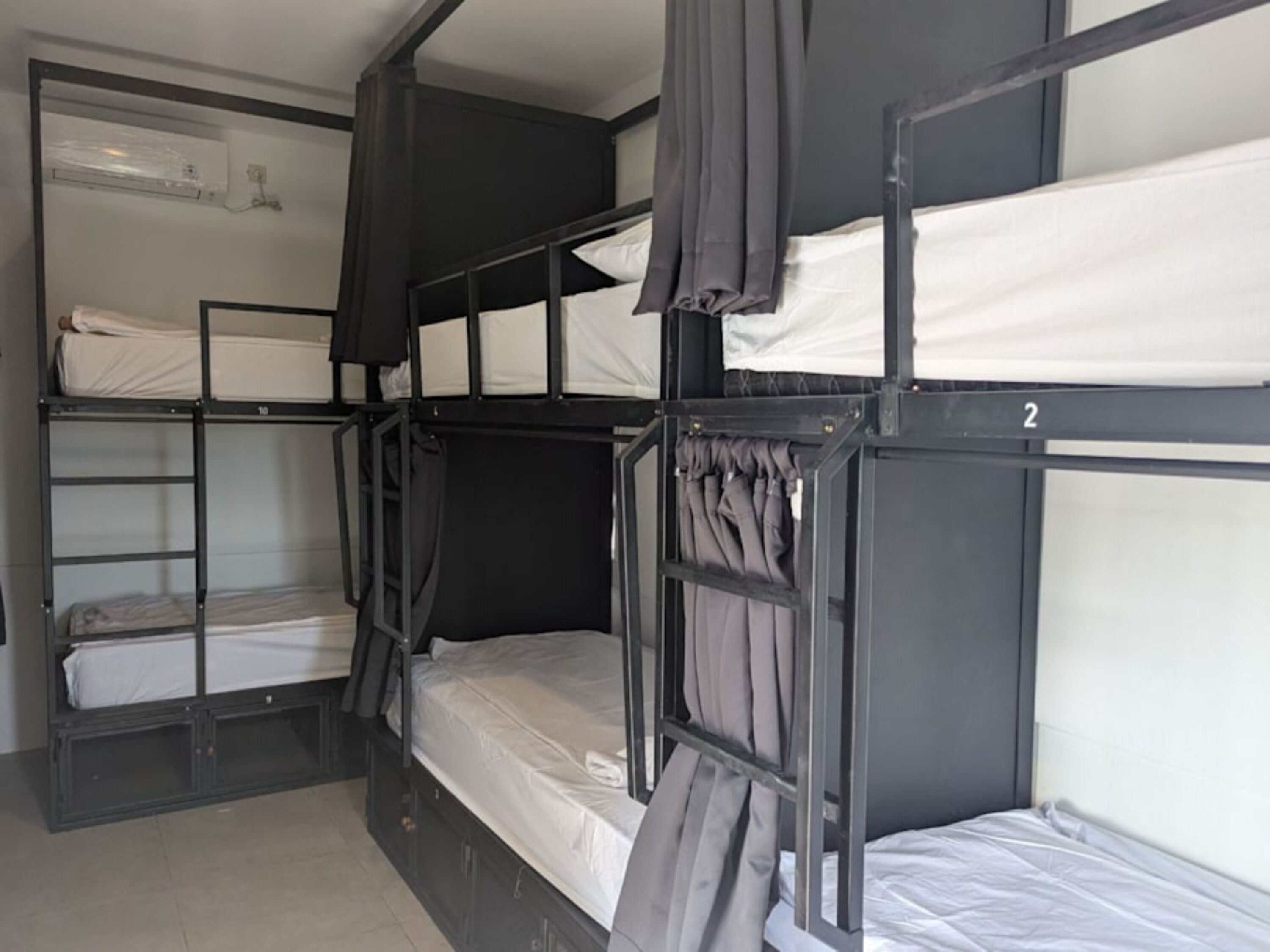 A bunk bed room with two beds, a small shelf, and a window with curtains.