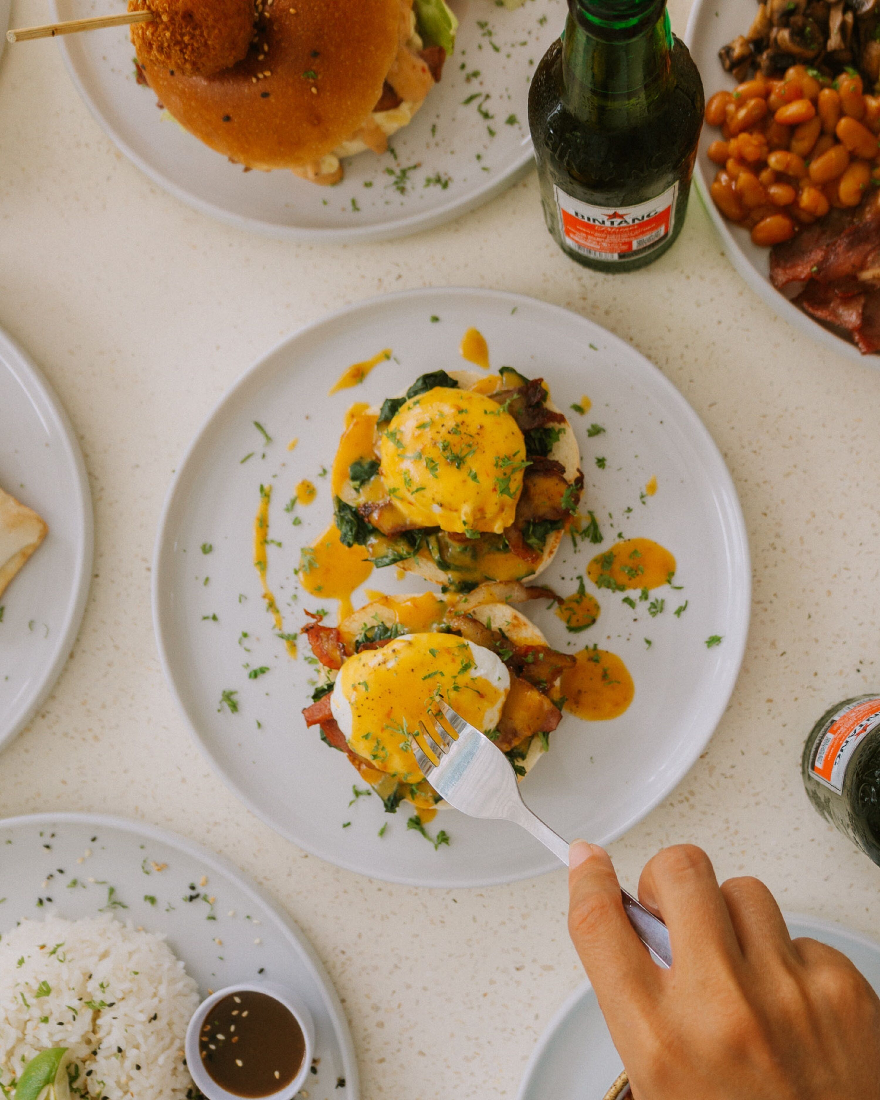 Una mesa de comedor con platos de comida, incluyendo huevos, frijoles y una botella de cerveza.