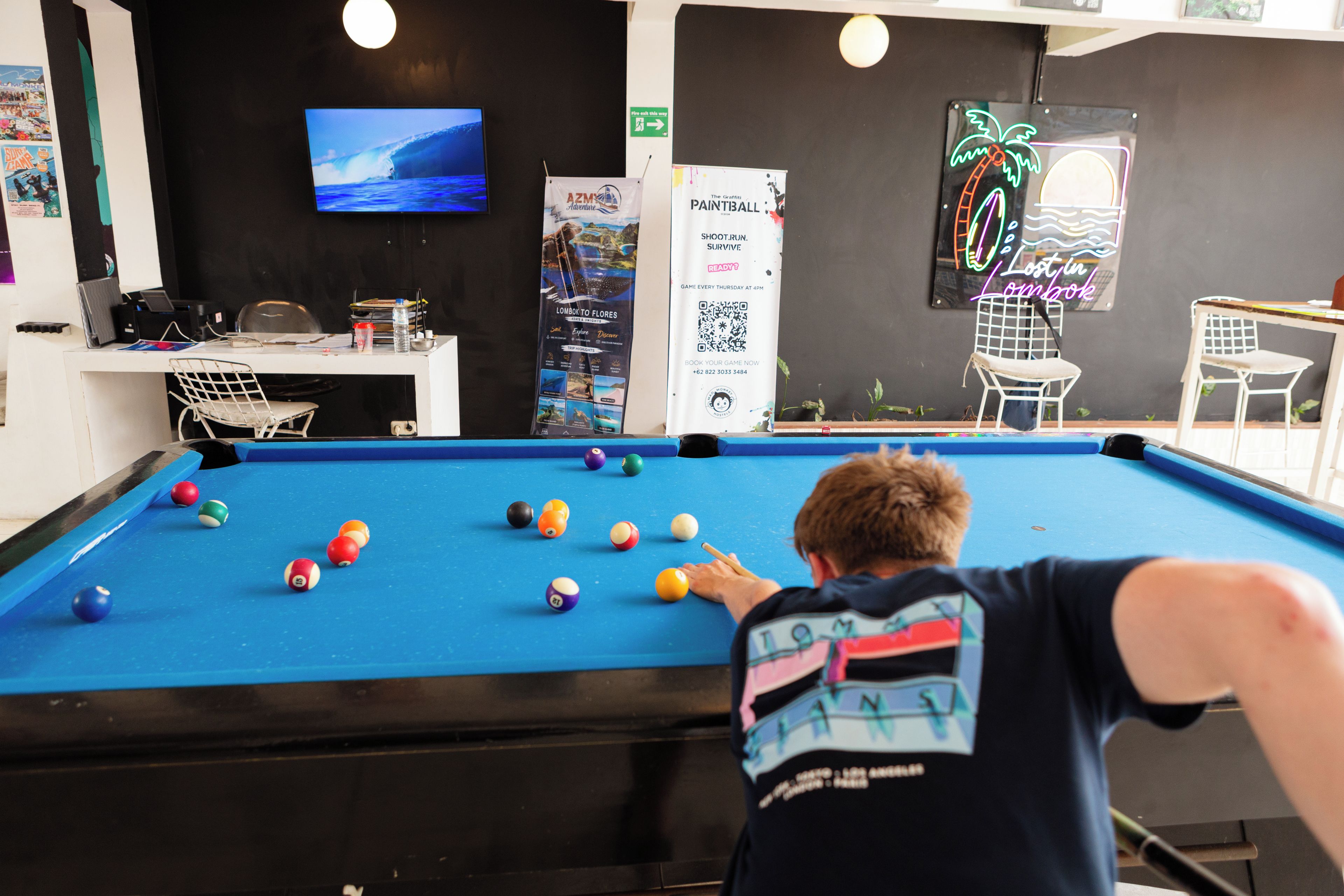 A pool table with billiard balls, a television mounted on the wall, and a neon sign.