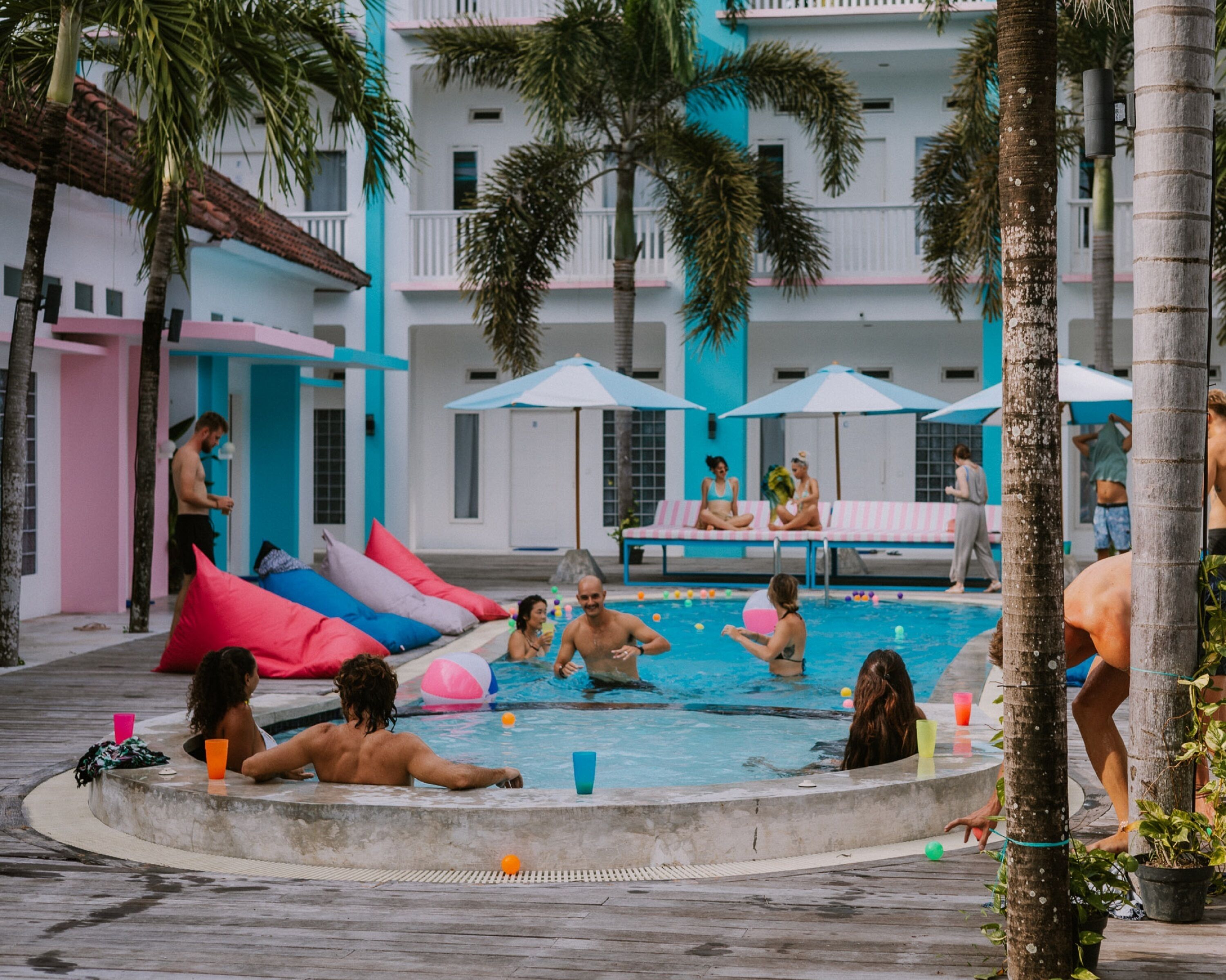 A pool area with lounge chairs, palm trees, and a building with balconies.