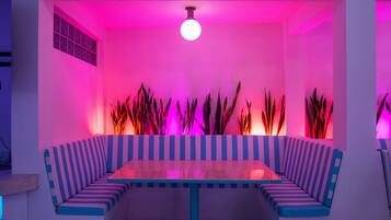 Une pièce moderne et lumineuse, avec un banc à rayures et une table, entourée de grandes plantes et agrémentée d’un luminaire au plafond original.
