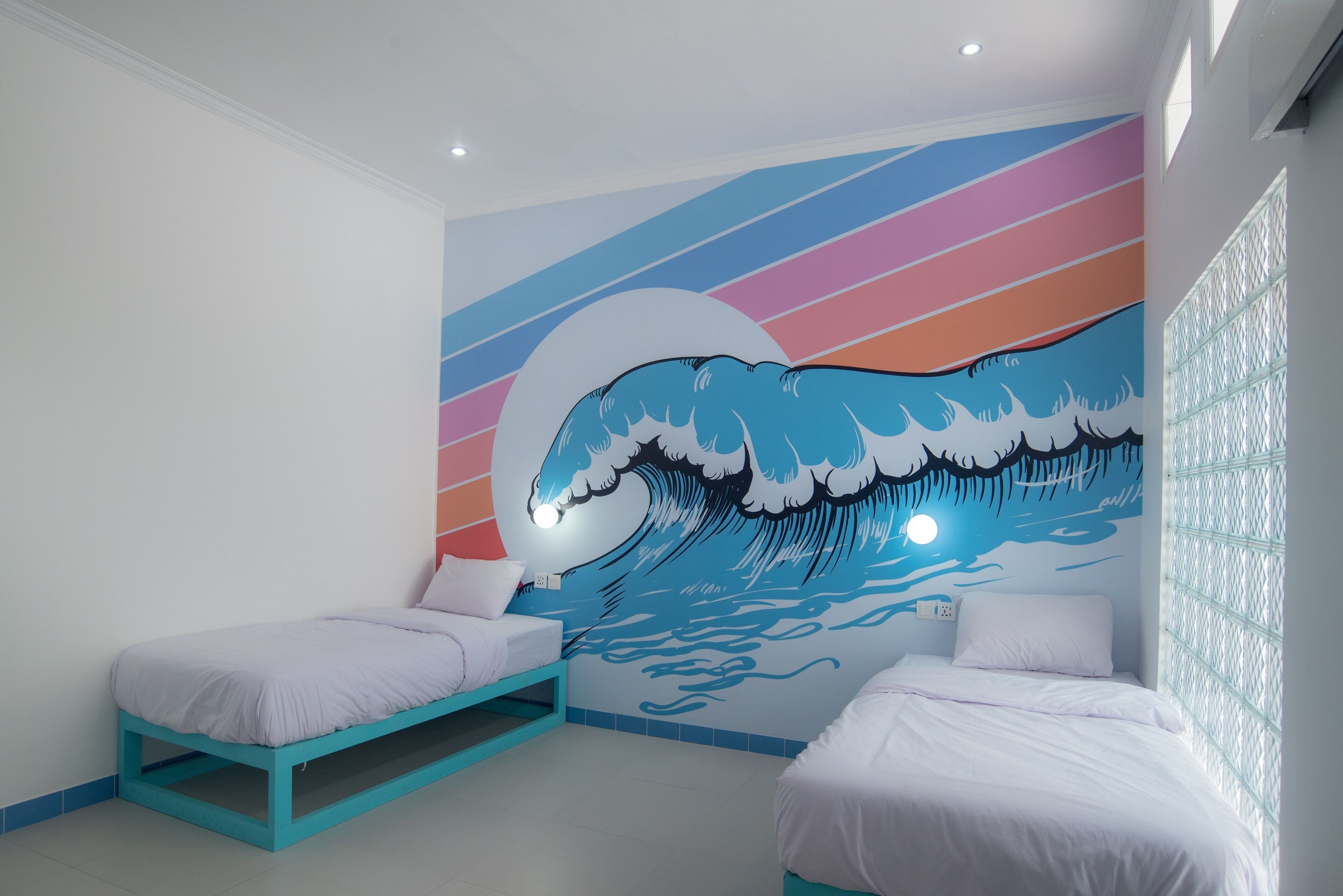 Een kamer met twee bedden, waarvan één een blauw frame heeft, en een grote muurschildering van een golf.