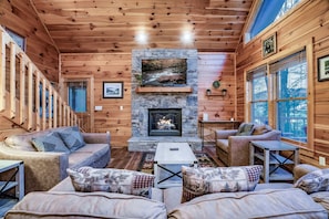 A cozy cabin interior with a stone fireplace, wooden walls, and a sofa with patterned cushions. - ★Cozy Cabin with Hot Tub, Game Room, and Fire pit!★ Wears Valley! (Sevierville)