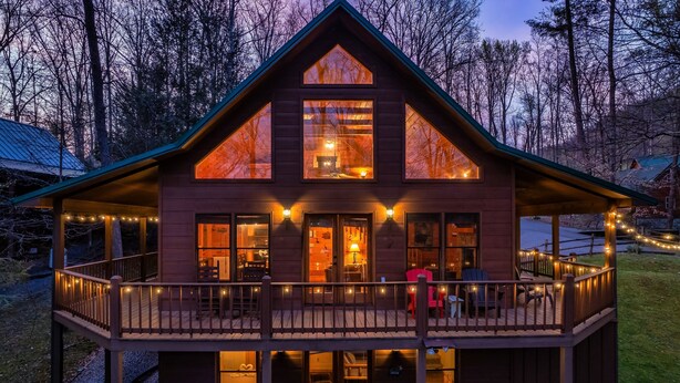 A two-story wooden cabin with a balcony, a hot tub, and string lights. - ★Cozy Cabin with Hot Tub, Game Room, and Fire pit!★ Wears Valley! (Sevierville)