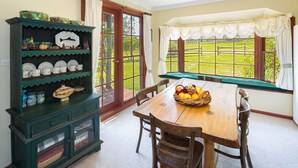 A dining area with a wooden table, chairs, a fruit basket, and a green cabinet with dishes. - Moffat Falls Lodge (Ebor)