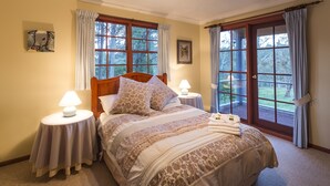 A bedroom with a large bed, two bedside tables with lamps, a wooden headboard, and a view of the outdoors through large windows. - Moffat Falls Lodge (Ebor)