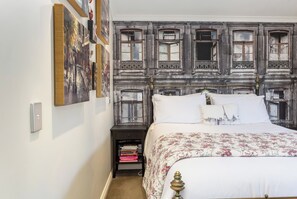 A bedroom with a bed, a nightstand with books, and a wall with framed pictures.