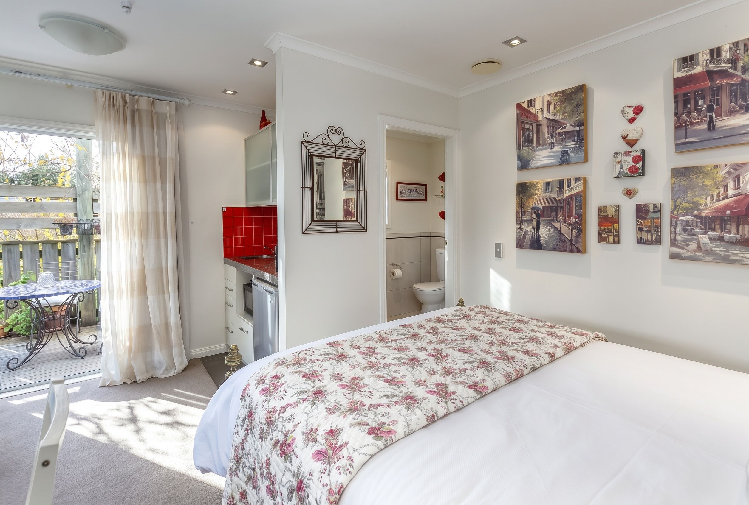 A bedroom with a bed, a bathroom, a dining area with a table and chairs, and a view of the outside.