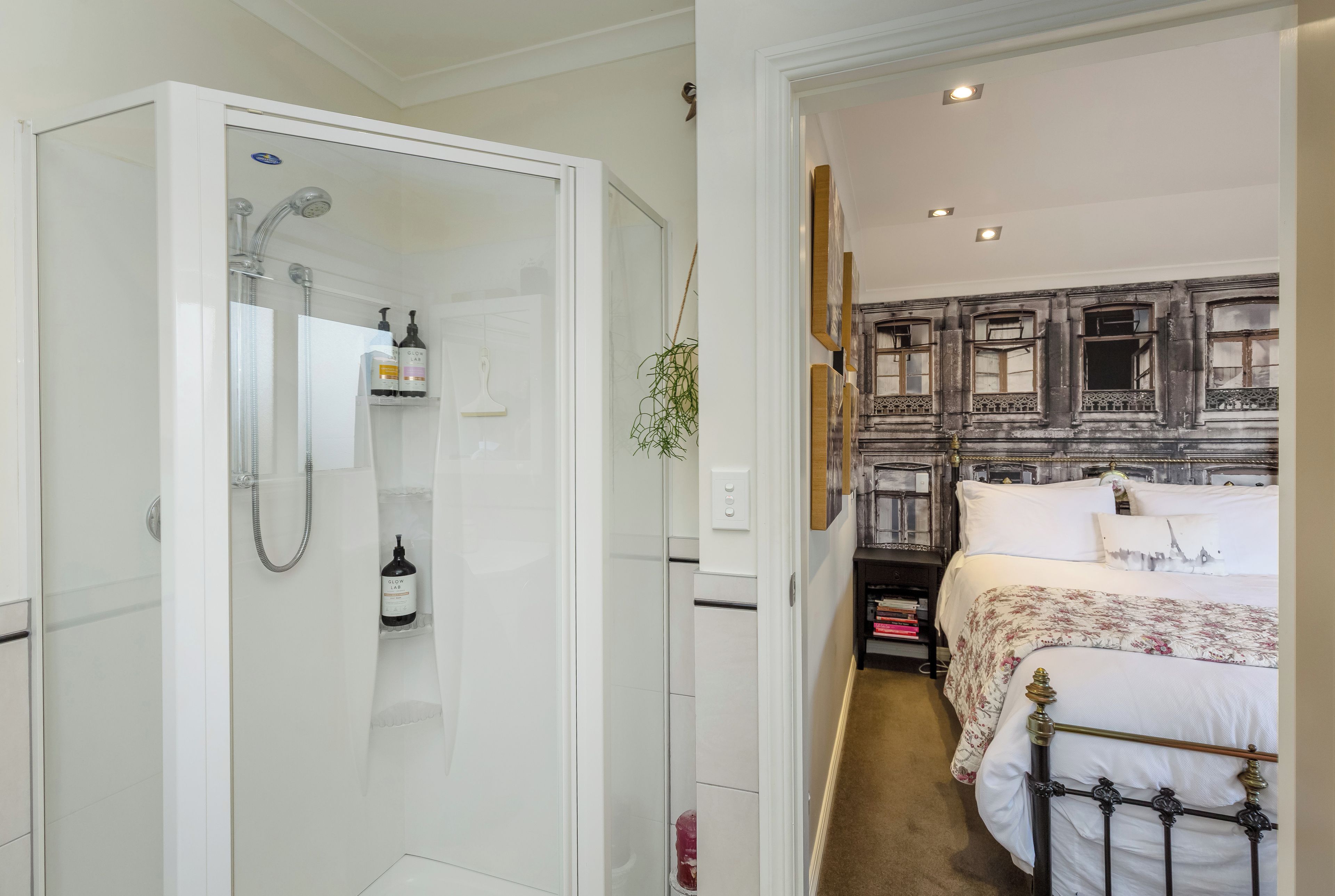 Une salle de bain avec une douche, des toilettes et un lavabo. On y trouve un lit avec une tête de lit et une table de chevet avec une lampe.