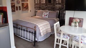 Een slaapkamer met een bed, een witte stoel, een klein tafeltje en een televisie.