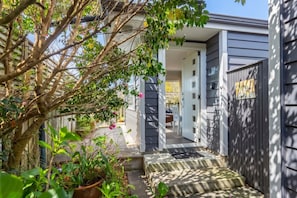 A residential property with a covered outdoor area, a staircase leading to the entrance, and a garden with potted plants.