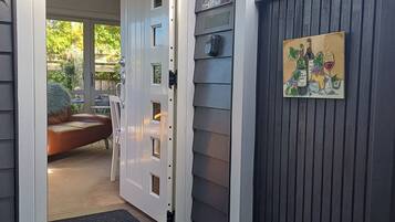Une porte qui donne sur une pièce offrant une vue sur un jardin et où se trouve un canapé en cuir marron.