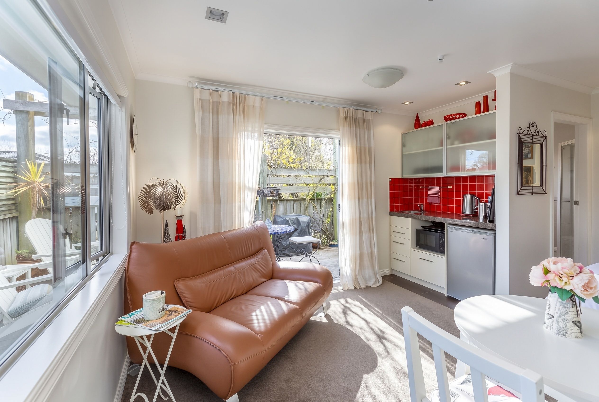A modern living room with a leather sofa, a dining table, and a kitchen area with red tiles.