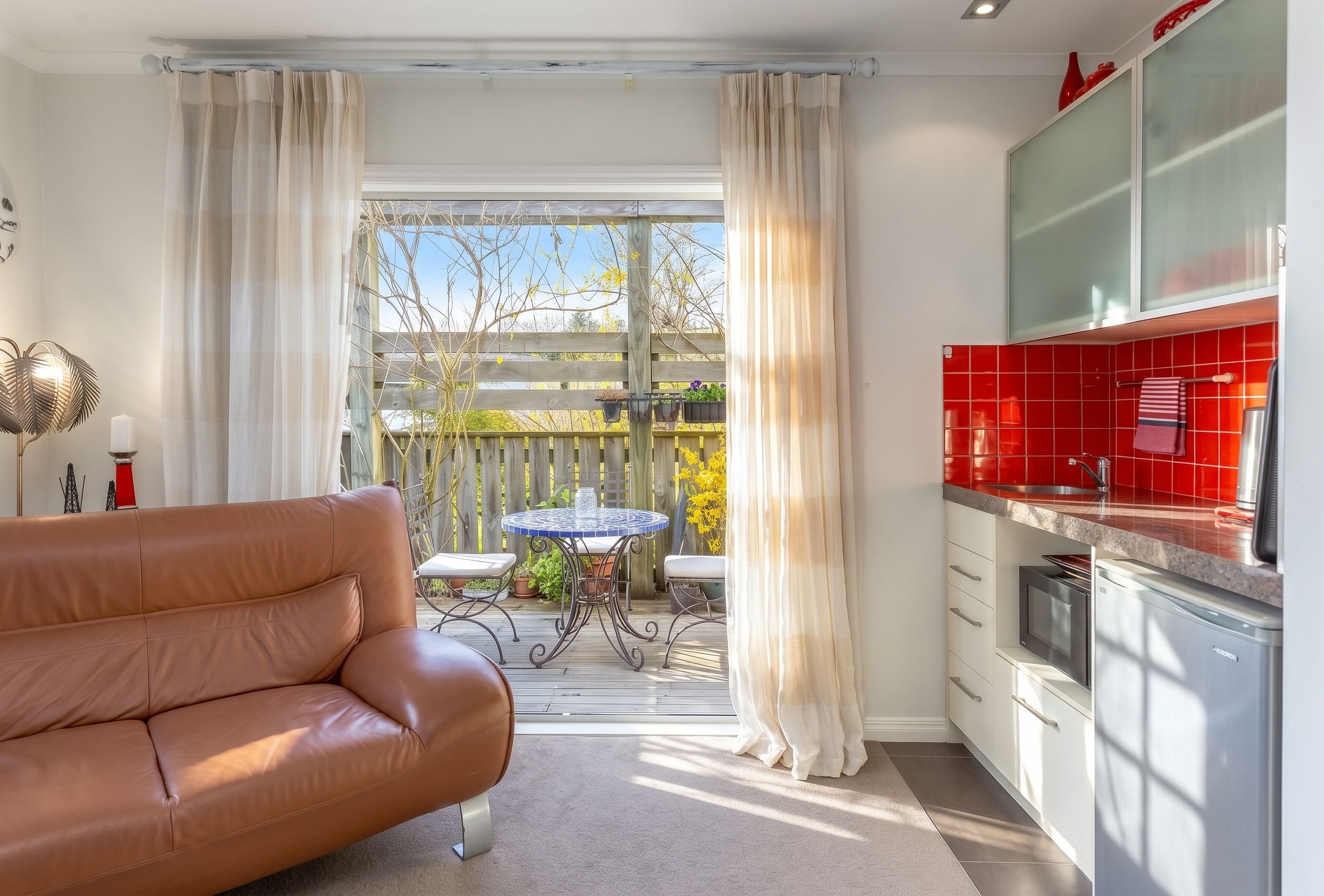 A modern kitchen with red tiles, a dining area with a table and chairs, and a leather sofa.
