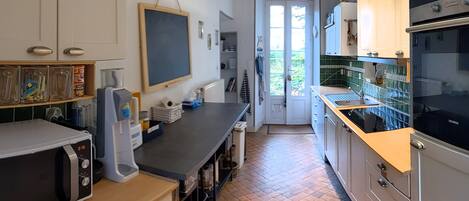 A compact kitchen with a microwave, a Siemens oven, and a sink. There is a chalkboard on the wall and a door leading to a balcony.