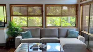 Un salón con un sofá seccional beige, una mesa de centro de vidrio y un ventanal con vistas a zonas verdes.