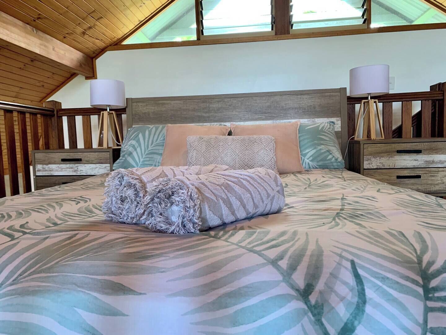 A bedroom with a bed, two bedside tables, a headboard, and a skylight.