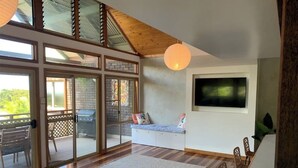 Amplia sala de estar con grandes puertas corredizas de vidrio que dan a un balcón, un televisor de pantalla plana montado en la pared y techo de madera.