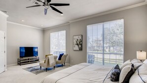 A bedroom with a large bed, a TV, a ceiling fan, and large windows. - Big 5 Bed/ 3.5 Bath Modern Home ⌂ Disney+ included, Free Parking, Fast Wi-Fi (Plano)