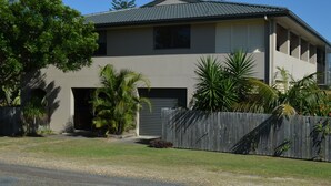 A two-story house with a garage, surrounded by a wooden fence and various tropical plants. - 'SEASIDE RETREAT' beach & nature at your doorstep (Wooli)