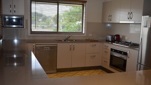 A modern kitchen with a dishwasher, stove, oven, and a window with blinds. - 'SEASIDE RETREAT' beach & nature at your doorstep (Wooli)
