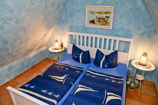 A bedroom with a bed, two bedside tables, a nightstand, a wall-mounted picture, and a small table with a lantern.