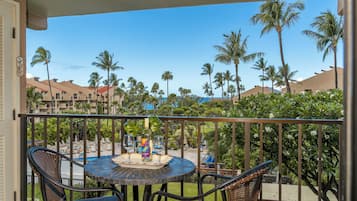 A balcony with a round table and two chairs, overlooking a pool area with palm trees and a clear blue sky.