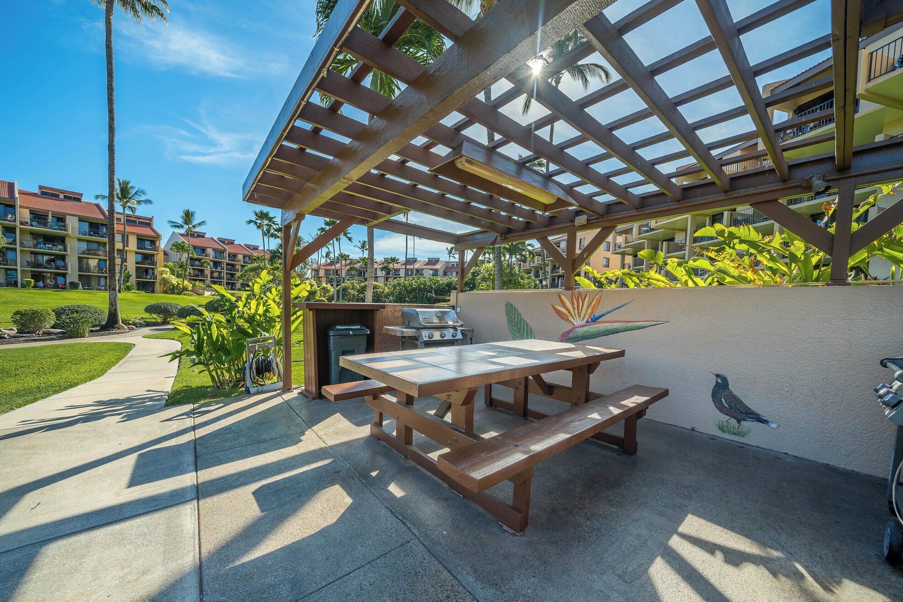 Un patio exterior con una mesa y bancos de madera, rodeado por una pérgola.