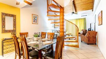 A dining area with a glass table, wooden chairs, and a spiral staircase.