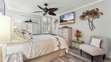 A bedroom with a bed, a chair, a dresser, a TV, and a ceiling fan.