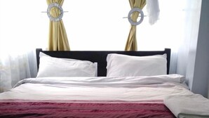 Een net opgemaakt bed met wit en bordeauxrood beddengoed, een donker hoofdbord en twee ronde decoraties aan de muur.