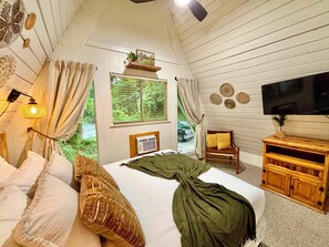 A bedroom with a bed, a television, a chair, and a window with a view of greenery. - Renovated Charming A-frame in Chalet Village! GSMNP! Hot Tub! Arcade! Bears! (Gatlinburg)