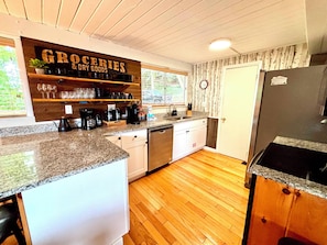 Una cocina con suelo de madera, encimera de granito, lavavajillas y refrigerador.
