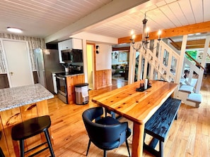 A kitchen with a wooden table, chairs, and a trash bin. - Renovated Charming A-frame in Chalet Village! GSMNP! Hot Tub! Arcade! Bears! (Gatlinburg)