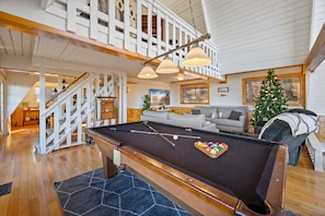 A pool table in a room with a staircase, a Christmas tree, and a sofa.