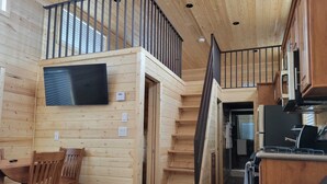 A wooden cabin interior with a dining area, kitchen, and a staircase leading to a loft. - 079 Tiny Home near Grand Canyon South Rim Sleeps 8 (Williams)