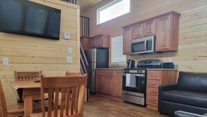 A compact kitchen with wooden cabinets, a microwave, a stove, and a refrigerator. - 079 Tiny Home near Grand Canyon South Rim Sleeps 8 (Williams)