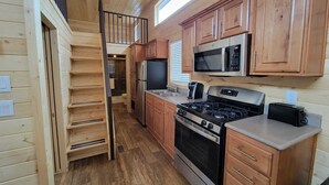 A compact kitchen with wooden cabinets, a microwave, a stove, and a toaster. - 079 Tiny Home near Grand Canyon South Rim Sleeps 8 (Williams)
