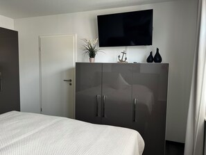 A bedroom with a bed, a wardrobe, a television, and a potted plant.