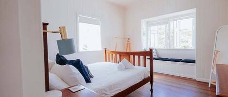 Un dormitorio con cama de madera, una mesita de noche, un ventanal con vistas y un ventilador de techo.