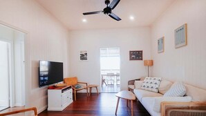 Una sala de estar con televisor, sofá, sillas y ventilador de techo.